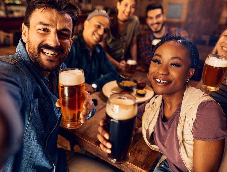 Group of happy friends having fun while drinking beer and taking selfie in a bar.